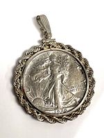 Front of silver pendant with 1920 Standing Liberty Half Dollar coin, showing Liberty walking and the inscription 'IN GOD WE TRUST'.