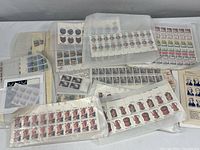 Wide view showing multiple sets of U.S. postage stamp plate blocks on table, mostly in translucent glassine envelopes.
