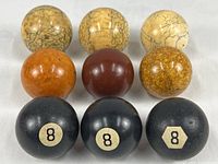 All nine balls shown together grouped, includes three vintage black billiard 8-balls and six polished stone balls in natural earth tone colors.