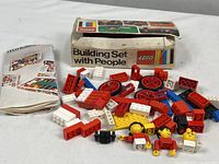 Photo of scattered LEGO bricks, vintage LEGO people, original worn box, and instruction booklet on a white surface.