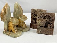 Two pairs of stone bookends: on the left, the onyx pair depicts stylized figures; on the right, the soapstone pair features carved floral motifs in relief.