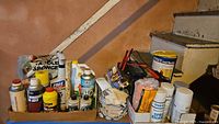 Box and containers of automotive chemicals, gloves, battery charger, sponges, and spray paint cans arranged on a basement stairway