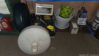 Photo showing 2 umbrella bases, garden pots, small solar outdoor lantern light, garden tools scattered and bug repellent spray in a basement setting