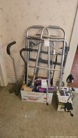 Two aluminum walkers, two canes, and boxes with various health care supplies on carpet by wall