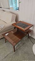 Side view of the midcentury modern wooden end table with raised glass top showing zodiac tiles and tapered legs.