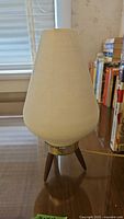 Side view of the lamp showing tapered ribbed white glass shade and wooden tripod base
