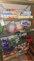 Shelving units with assorted kitchen and cleaning items, including plastic containers, glass pie plates, paper products, cleaning pads and sprays.