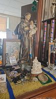 Wide view of religious items showing St. Anthony chalkware statue, rosaries, coins, medallions, and pictures behind