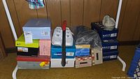 Multiple stacked shoe boxes with various branded boxes visible including Basic Editions, assorted women's shoes, shoe horn on top