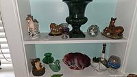 Shelf display of all vintage ceramics, glassware and figurines in lot, showing ceramic urn vase, Homeco horse and bear, slag glass bowl, lighthouse, candle holders and small glass items