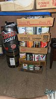Image showing stacked vintage beer cans with labels such as Michelob, Coors Light, Tulip, and other Canadian brands in cardboard and wooden carriers, along with two mini kegs.