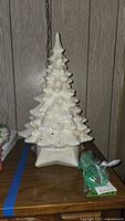 Front view of vintage ceramic Christmas tree with iridescent white glaze, showing star-shaped base and attached electrical cord, with green bird-shaped pegs packaged nearby.