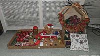Overview photo showing assortment of vintage Christmas decorations arranged in trays and floor including a decorative pillow, ornaments, figurines, and greenery candle rings.