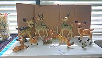 Wide view of all animal figurines arranged on table against cardboard backdrop, showing the collection of deer, dog, chicken, and duck figurines.