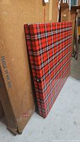 Full view of folded table with plaid pattern leaning against storage boxes