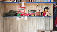 Wide shot of shelf with all vintage toys visible including Zip the monkey, Planter's Peanuts football jewelry box, Mustang picture, tin Camaro, dinosaur, and tank