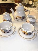 Front view of teapot, sugar bowl, creamer, two cups and saucers showing floral pattern and condition
