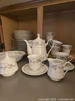 Overview of set: plates stacked, teapot, sugar bowl, creamer, cups and saucers displayed