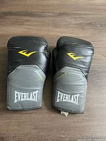 Front side of the pair of Everlast 16oz boxing gloves showing black and gray design with yellow and white logos.
