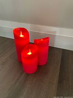 Three red LED flameless candles with different heights arranged on a floor, lit with visible moving flame effect.