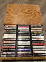 Wooden case holding three rows of cassette tapes placed on a floor.