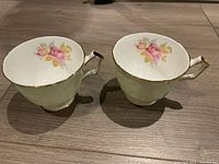 Pair of Aynsley bone china teacups with pink rose floral pattern and gold trim, shown from side.