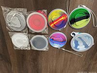 All eight silicone collapsible cups laid out, showing their colors and lids still in protective packaging. Four are solid colors grey, red, white, and black, and four are tie-dye pattern colors.