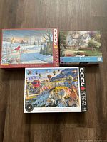 Three puzzle boxes displayed: Eurographics 'Country Cardinals', Eurographics 'Hot Air Balloons Cappadocia Turkey', and Thomas Kinkade puzzle.