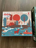 Box of 1000-piece puzzle featuring retro style camping scene with trees, tent, moose and canoe