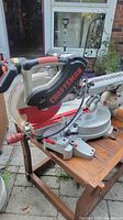 Front angle showing miter saw with Craftsman branding on blade guard, blade and base scale visible, mounted on wooden table outside.