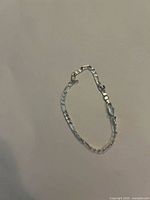 Photo showing a small silver bracelet with rectangular links laid against a light background.