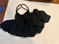 Black swimsuit cover, spread out showing full front view, highlighting gathered skirt and straps.