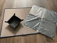 Foldable puzzle board partially open on wooden floor with one sorting tray placed on it, showing grey felt surfaces and folding segments