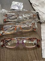 Three pairs of Tishui blue light blocking reading glasses sealed in plastic, various colored rectangular frames, on table with cleaning cloth and pouch