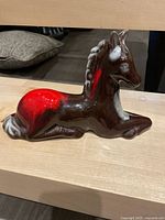 Side view of the brown and red Canadiana Pottery horse figurine lying down, showing glossy ceramic finish and sculpted mane detail.