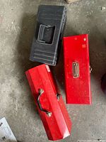 Two red Mastercraft metal tool boxes and one black Holt plastic tool box placed on a concrete surface.