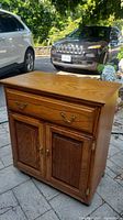 Front view of wheeled oak cabinet showing drawer and double door storage below.