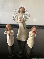 Front view of three Willow Tree angel figurines: a tall 9-inch angel with bouquet, a smaller angel holding hearts, and another smaller angel with clasped hands.