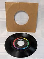 Black 7-inch vinyl record with rainbow Capitol label, accompanied by plain brown paper sleeve.