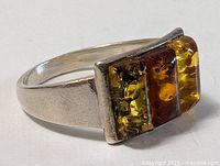 Front angle side photo showing the sterling silver band and trio of differently colored rectangular amber stones set in a flat bezel setting.
