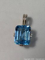 Front view of pendant showing rectangular emerald-cut blue topaz stone and silver setting with double bail.