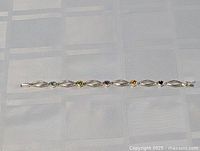 Full view of the 7-inch sterling silver bracelet with alternating open links and heart-shaped stones in multiple colors laid out flat on a light checkered fabric.
