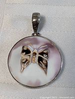 Photo of a round sterling silver pendant with carved butterfly design in abalone shell showing natural shell color variations with lavender hues.