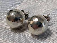 Close-up of pair of sterling silver hammered round dome stud earrings on fabric background, showing texture and shape.