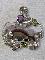 Close-up photo of handmade sterling silver pendant with multiple stones including amethyst, aqua blue topaz, peridot, and natural agate geode with druzy crystals
