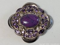 Top view of the large sterling silver pin brooch showing central oval cabochon purple stone and surrounding faceted amethyst stones.