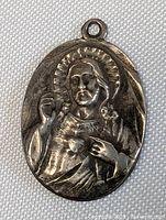 Front view of oval sterling silver pendant charm showing detailed relief of Jesus Christ with halo and sacred heart, dark patina finish.