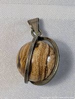 Front angle view of oval brown polished stone pendant set in sterling silver frame.