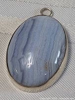 Front view of the polished oval blue lace agate pendant displaying its banded stone pattern and silver frame.