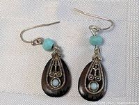 Close-up photo of a pair of tribal-style sterling silver earrings with wood teardrop bases and blue stones.